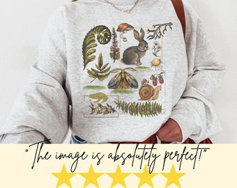 May include: A gray sweatshirt with a graphic print of a rabbit, a moth, a snail, a frog, and various plants. The graphic is in a collage style with a vintage aesthetic.