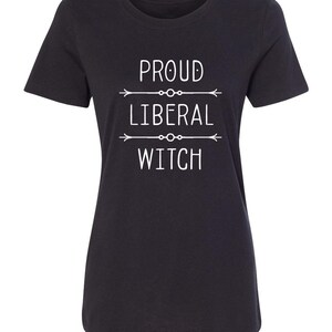 May include: Black t-shirt with white text that reads "PROUD LIBERAL WITCH" with arrows above and below the text.