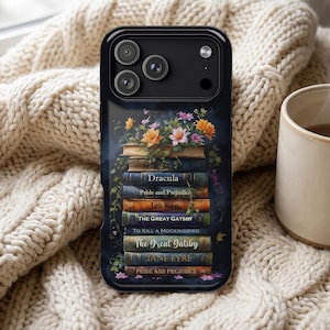 May include: A black smartphone case featuring a graphic illustration of a stack of vintage books topped with colorful flowers. The book spines are labeled with titles including Dracula, Pride and Prejudice, Little Women, The Great Gatsby, and Jane Eyre.