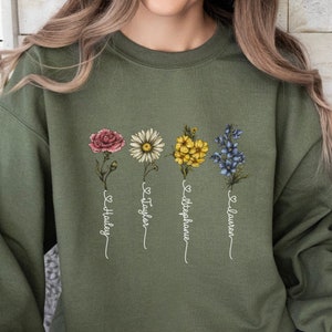 Pu&ograve; includere: Una felpa verde con un disegno floreale e i nomi "Hailey", "Taylor", "Stephanie" e "Lauren" scritti sotto i fiori.
