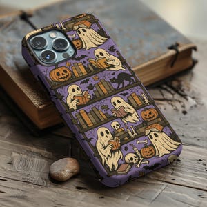 May include: A purple phone case featuring a Halloween-themed design. The case depicts ghosts reading books on shelves, with pumpkins, bats, and a black cat. The design has a cartoonish style, perfect for the spooky season.