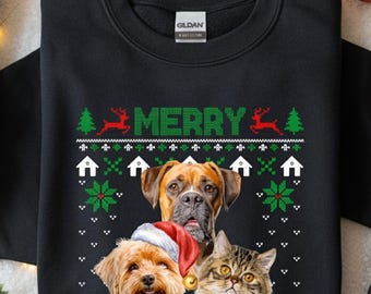 May include: Black sweatshirt with a festive design featuring a dog, cat, and dog wearing a Santa hat. The word "MERRY" is displayed in green above the animals, with reindeer and Christmas tree graphics. The sweatshirt has a crew neck.
