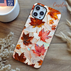 May include: A phone case featuring a stained-glass design with autumn maple leaves in shades of red, orange, and brown. The leaves are set against a white background with gold-colored outlines. The case has a black border and the text "Caseline".