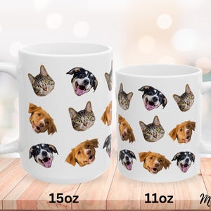 May include: Two white ceramic mugs with different sizes, 11oz and 15oz, featuring a pattern of various animal faces, including cats and dogs. The mugs are on a wooden surface.