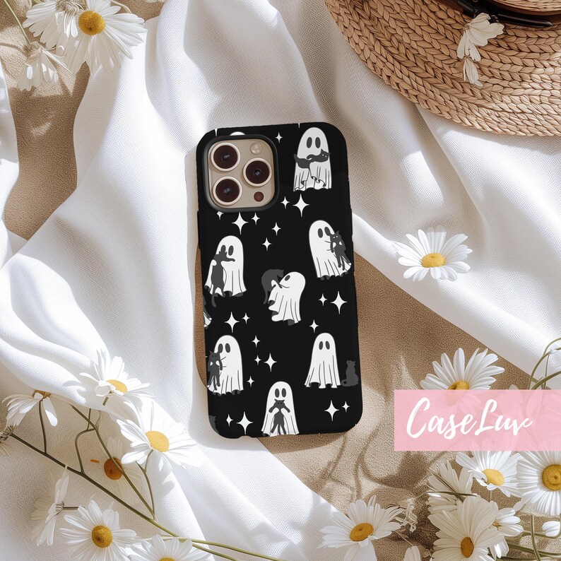 May include: Black phone case featuring a pattern of white ghosts and black cats with star accents. The case has a glossy finish and is surrounded by white daisies and a white fabric background. The text "Case Luv" is in the lower right corner.