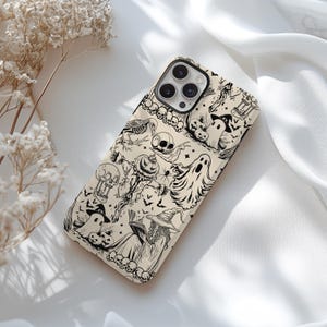 May include: A phone case with a Halloween-themed design. The case features a repeating pattern of black and white illustrations, including ghosts, skulls, bats, and witches. The case is beige and has a glossy finish.