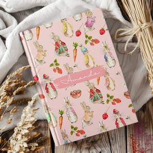 May include: A pink notebook with a repeating pattern of bunnies and strawberries. The name "Amanda" is written in white script on the cover.