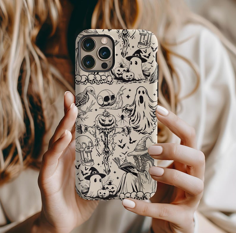 May include: Beige phone case with a black and white Halloween-themed pattern. The design includes ghosts, pumpkins, witches, skulls, and bats. The case is held by a person.