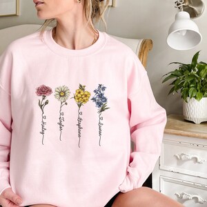 Pu&ograve; includere: Felpa rosa con un design floreale e i nomi Hadley, Taylor, Stephanie e Lauren scritti sotto i fiori.