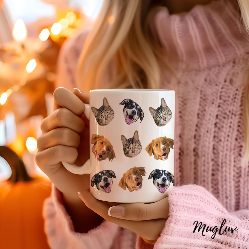 May include: White ceramic mug with a pattern of nine different pet faces. The faces include dogs and cats. The mug is being held by a person's hand.