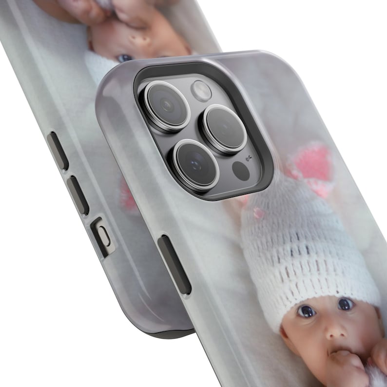 Peut inclure: Deux coques de t&eacute;l&eacute;phone avec une photo de b&eacute;b&eacute; imprim&eacute;e. Les coques sont blanches avec un bord gris et une finition brillante. Le b&eacute;b&eacute; porte un bonnet en tricot blanc avec des d&eacute;tails roses et a les yeux bleus.
