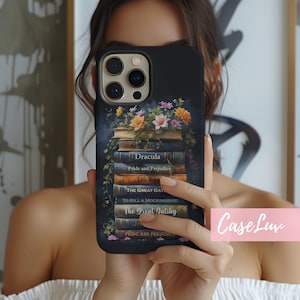 May include: Black phone case featuring a stack of classic books with titles like "Dracula" and "The Great Gatsby." The case is adorned with floral accents in shades of orange, pink, and green. The brand name "CaseLuv" is displayed in a pink box.