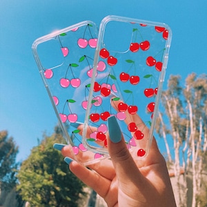 May include: Two clear phone cases with a cherry print. One case has pink cherries and the other has red cherries.