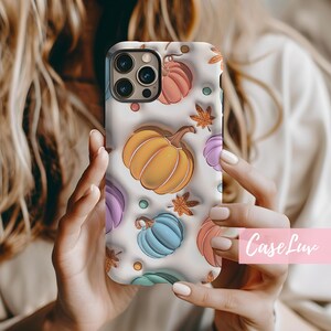 May include: A white iPhone case with a colorful autumn-themed design featuring pumpkins, leaves, and dots.