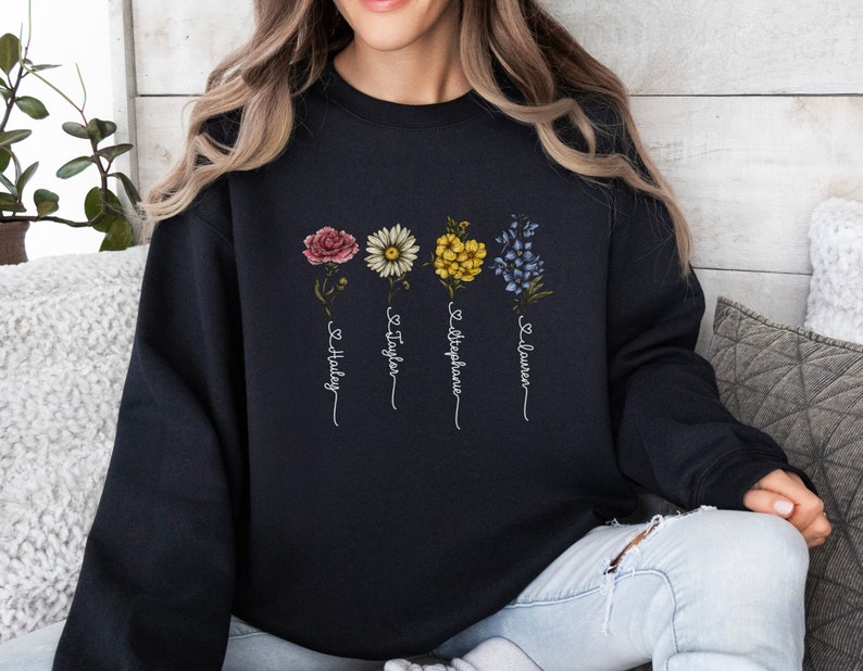 Pu&ograve; includere: Felpa nera con un design floreale e i nomi "Hailey", "Taylor", "Stephanie" e "Lauren" scritti verticalmente sotto i fiori.