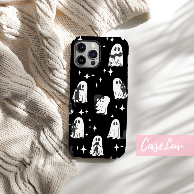 May include: Black phone case with a repeating pattern of white ghosts and stars on a black background. The phone case has a camera cutout and the text "Case Luv" in pink.