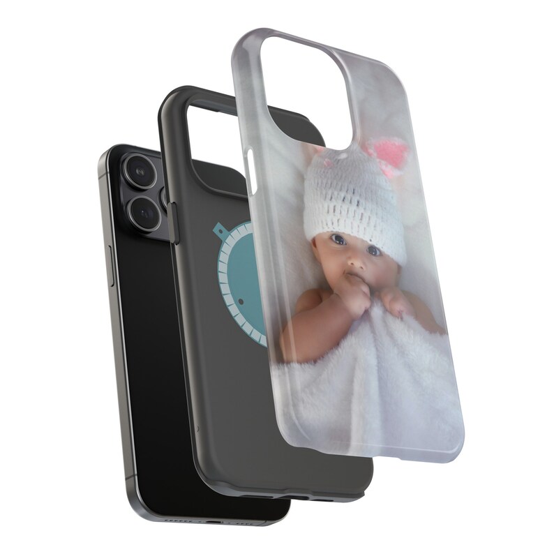 Peut inclure: Un smartphone noir avec une coque de protection repr&eacute;sentant un b&eacute;b&eacute; portant un bonnet blanc tricot&eacute; avec des accents roses. La coque est transparente et le b&eacute;b&eacute; est envelopp&eacute; dans une couverture blanche.