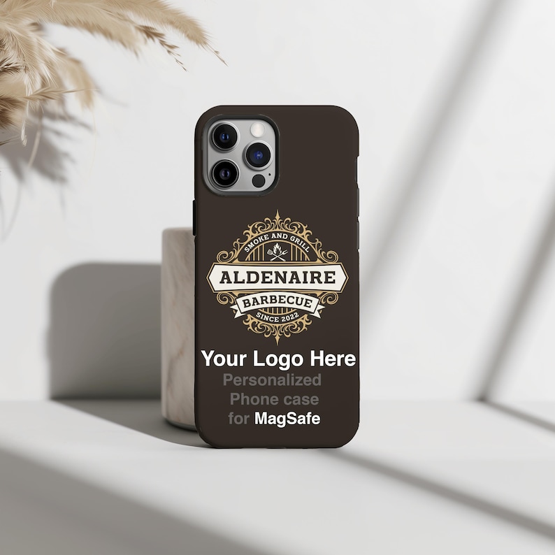 Peut inclure: Coque de t&eacute;l&eacute;phone marron avec le texte "ALDENAIRE BARBECUE SINCE 2022" dans un embl&egrave;me d&eacute;coratif. La coque pr&eacute;sente &eacute;galement le texte "Your Logo Here" et "Personalized Phone case for MagSafe".