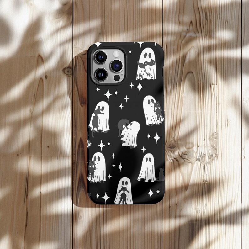 May include: Black phone case featuring a repeating pattern of white ghosts, black cats, and stars on a black background. The case has a glossy finish and a camera cutout. The design is perfect for Halloween.