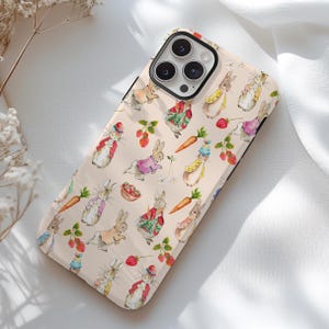 May include: A pink phone case with a repeating pattern of white rabbits, strawberries, and flowers. The phone case has a cutout for a camera lens.