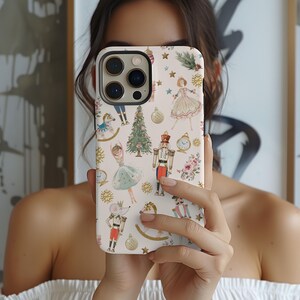May include: A white phone case with a Christmas Nutcracker theme. The case features a repeating pattern of nutcrackers, ballerinas, Christmas trees, and other festive elements. The case is designed for an iPhone.