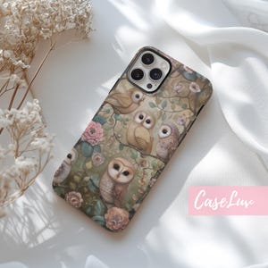 May include: A phone case with a floral design featuring owls in shades of brown, white, and gray. The case has a textured background with pink flowers and green leaves. The phone case is designed for an iPhone.
