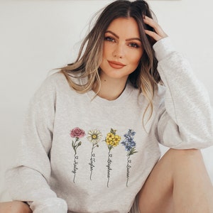 Pu&ograve; includere: Una felpa grigia con un disegno floreale e i nomi Hailey, Taylor, Stephanie e Lauren scritti verticalmente sotto i fiori.