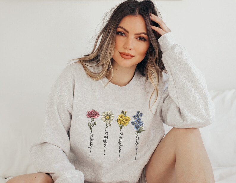 Pu&ograve; includere: Una felpa grigia con un disegno floreale e i nomi Hailey, Taylor, Stephanie e Lauren scritti verticalmente sotto i fiori.