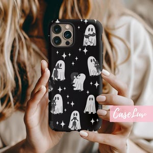 May include: Black phone case featuring a pattern of white ghosts and star shapes. The ghosts have various designs, some with cats. The case has a glossy finish and a camera cutout. The text "Case Luv" is in the bottom right corner.