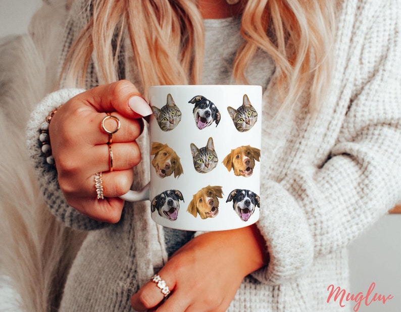 May include: White ceramic mug with a repeating pattern of dog and cat faces. The mug is being held by a person's hand.