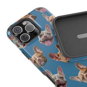 May include: A blue phone case featuring a repeating pattern of smiling French Bulldog faces. The case has a black border and a camera cutout. The dogs are various shades of brown and tan.