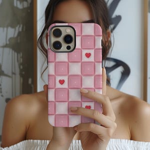 May include: A pink and white checkered phone case with three red hearts. The case is designed for an iPhone.
