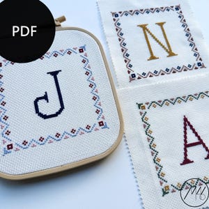 Peut inclure: Trois cerceaux à broder avec des motifs de point de croix représentant les lettres J, N et A. Les lettres sont entourées d'une bordure géométrique colorée.