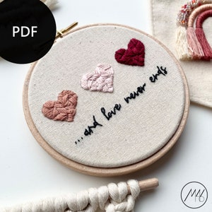 Op de afbeelding: Borduurkunst in een hoepel met drie roze, rode en oranje harten en de tekst "...en liefde eindigt nooit".