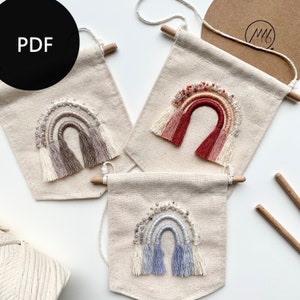 Può includere: Tre striscioni in tela con disegni a forma di arcobaleno. Ogni striscione presenta un arcobaleno fatto di filato con accenti di perline e nappe. Gli arcobaleni sono in tonalità beige, rosso e blu.