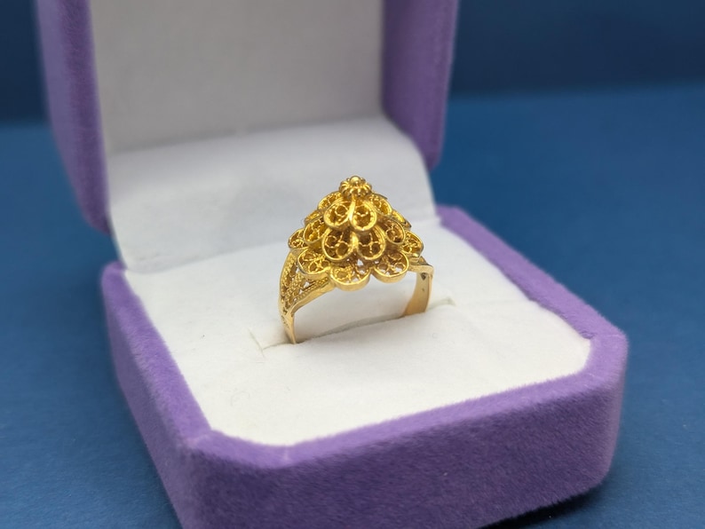 May include: A gold ring with a delicate, intricate design. The ring is in a purple velvet ring box.