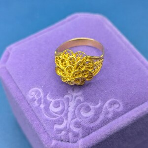 May include: A gold filigree ring with a delicate, intricate design. The ring is displayed in a purple velvet ring box.