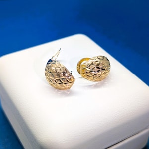 May include: A pair of gold hoop earrings with a textured, diamond-shaped pattern. The earrings are displayed on a white box.