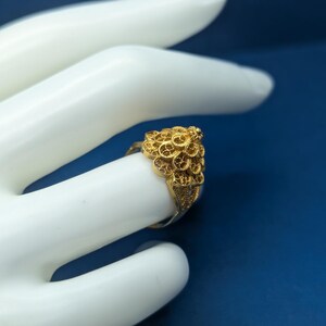 May include: A gold filigree ring with a detailed design. The ring is worn on a model's finger.