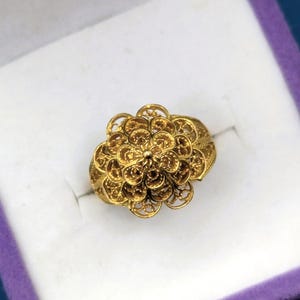 May include: A gold ring with a delicate floral design. The ring is made of intricate filigree work and has a round shape.