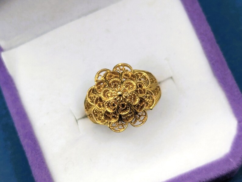 May include: A gold ring with a delicate floral design. The ring is made of intricate filigree work and has a round shape.