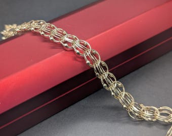 May include: A gold-colored bracelet with a series of interconnected oval links. Each link is composed of smaller, circular elements and small beads. The bracelet is displayed on a red box with a dark burgundy trim.
