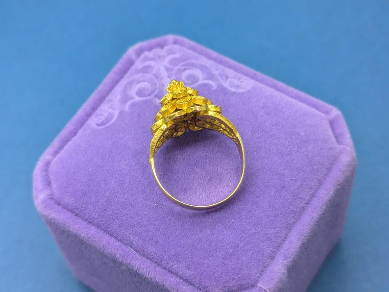 May include: A gold ring with a floral design. The ring is in a purple velvet ring box.