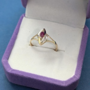Puede incluir: Un anillo de oro con una piedra preciosa de rubí rojo y pequeños diamantes engastados en un diseño en forma de hoja.