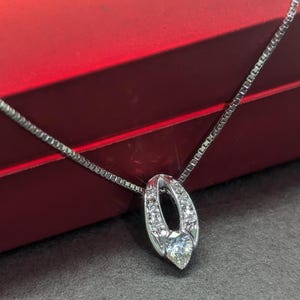 May include: A silver necklace with a diamond pendant in the shape of an oval. The pendant is set with small diamonds around the edge.