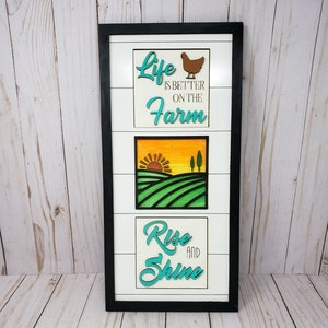 Könnte beinhalten: Ein gerahmtes Holzschild mit drei Tafeln. Die obere Tafel zeigt ein braunes Huhn und den Text "Life is better on the farm". Die mittlere Tafel zeigt einen Sonnenuntergang über einem grünen Feld. Die untere Tafel trägt den Text "Rise and Shine".