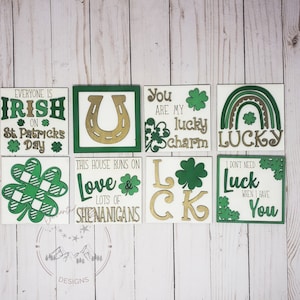 May include: Set of eight wooden signs with green and gold paint and shamrock designs. The signs feature various St. Patrick's Day themed phrases, including "Everyone is Irish on St. Patrick's Day", "This house runs on love & lots of shenanigans", "You are my lucky charm", "Lucky", "I don't need luck when I have you", and "LCK".