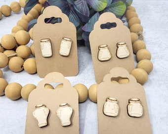 May include: Four pairs of wooden earrings with a mason jar design. The earrings are displayed on brown card stock with a hole at the top for hanging.