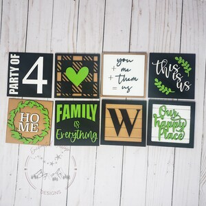 Puede incluir: Nueve letreros de madera con diseños pintados en negro y verde. Los letreros presentan frases como "Party of 4", "Home", "Family is Everything", "You + Me + Them = Us", "This is Us", "Our Happy Place", y un diseño de corazón.