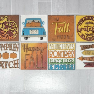 Op de afbeelding: Acht houten borden met herfstthema's. De borden bevatten pompoenen, een vrachtwagen en zinnen zoals "Happy Fall", "Ik hou van herfst" en "Pumpkin Patch".